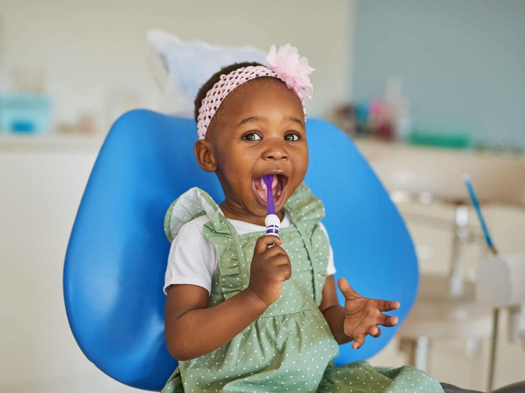 a child with a toothbrush in their mouth, at a pediatric dentist office